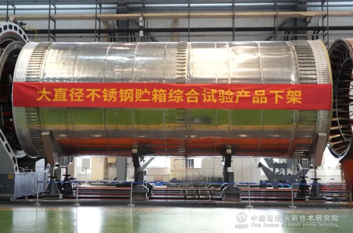 A large cylindrical stainless steel propellant tank, developed by the China Academy of Launch Vehicle Technology (CALT), sits mounted in a factory setting. A red banner across the tank reads “Large-diameter stainless steel tank integrated test product off the assembly line” in Chinese.