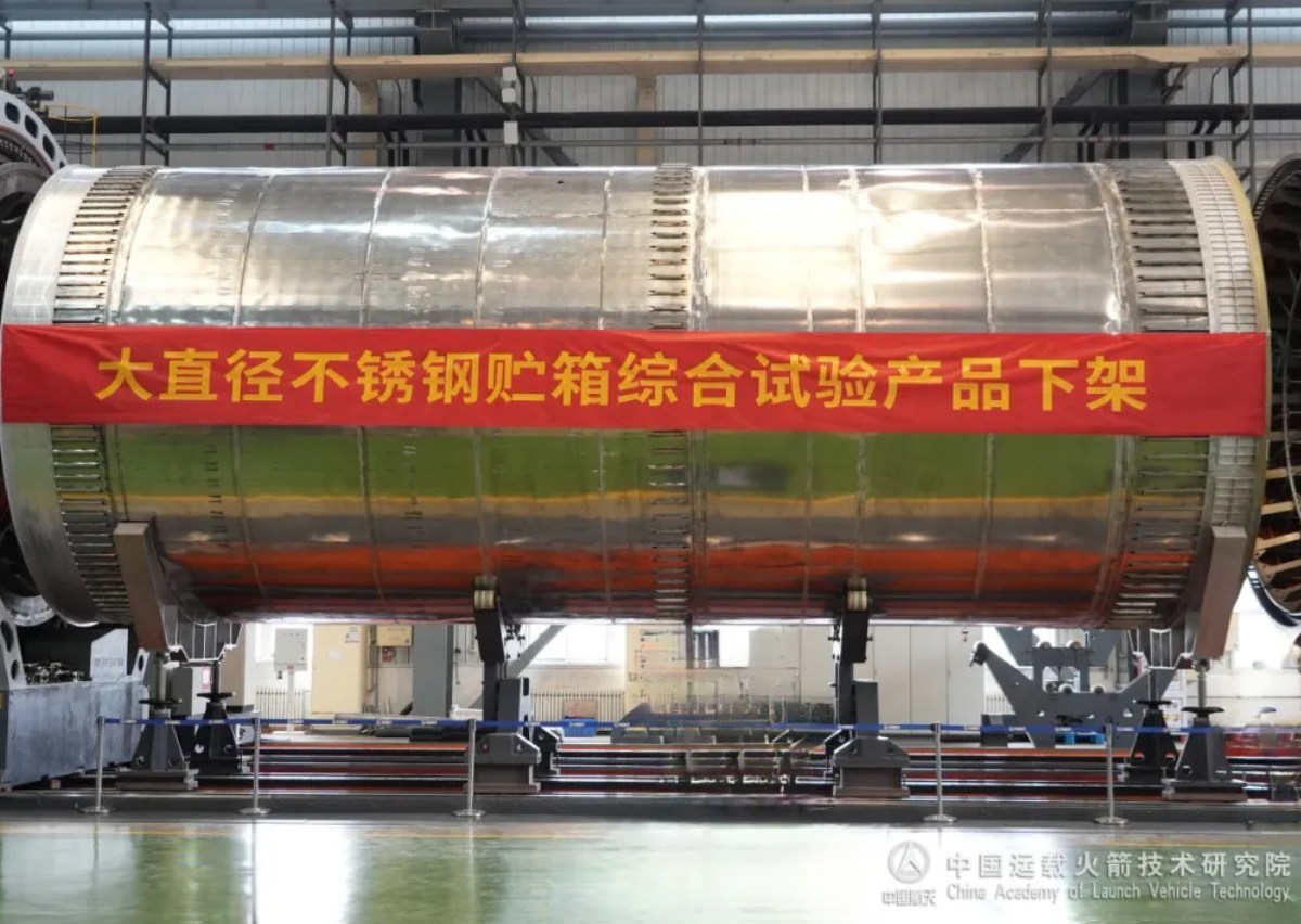 A large cylindrical stainless steel propellant tank, developed by the China Academy of Launch Vehicle Technology (CALT), sits mounted in a factory setting. A red banner across the tank reads “Large-diameter stainless steel tank integrated test product off the assembly line” in Chinese.