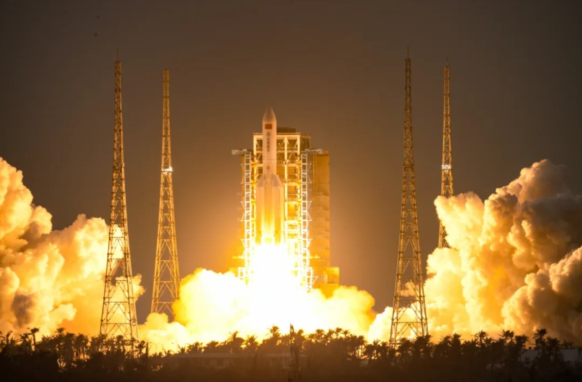 A dramatic nighttime launch of China's Long March 5B rocket from the Wenchang Space Launch Center on December 16, 2024. Bright orange flames and thick clouds of white smoke illuminate the launchpad as the rocket ascends into the sky, carrying the first 10 satellites for the Guowang ('national net') low Earth orbit communications megaconstellation. Tall support towers frame the scene against the dark backdrop, highlighting the power and scale of the mission.