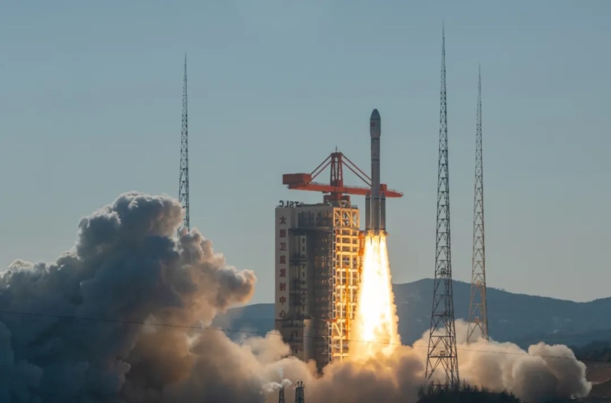 A Long March 6A rocket climbs above the launch tower at Taiyuan amid plumes of exhaust and a blue sky backdrop.